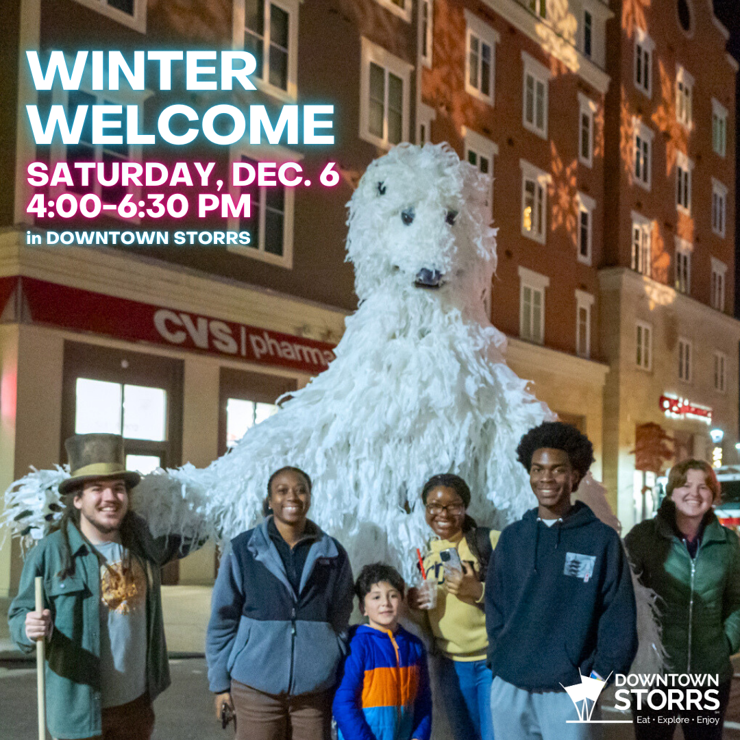A group of young adults and children smile as they stand in front of a 12-foot tall polar bear puppe
