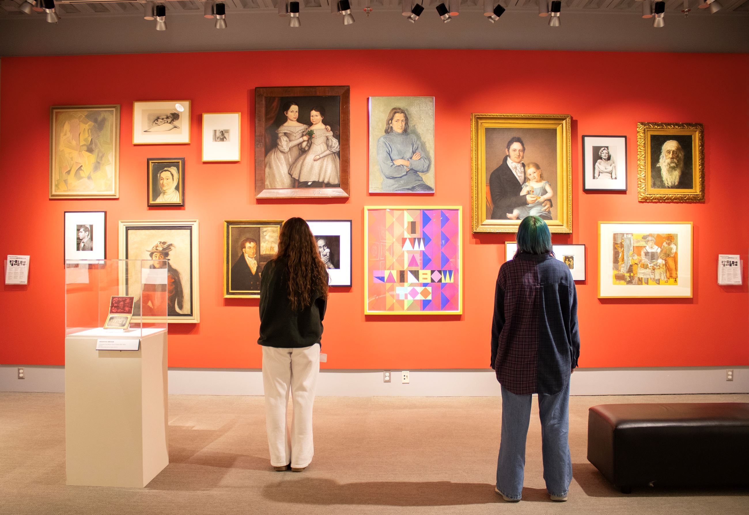 Two people stand and look at a gallery wall filled with portraits at the Benton Museum